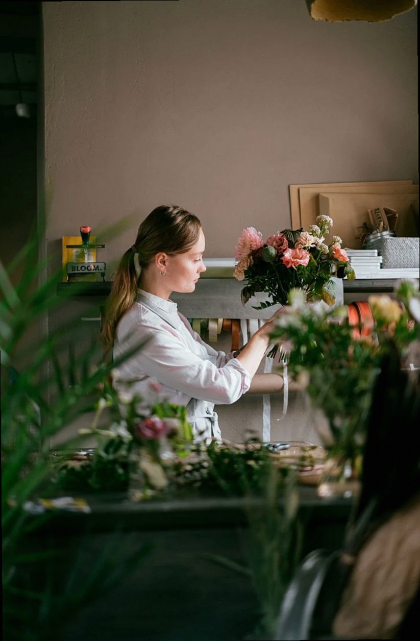 Florista profesional femenina arreglando flores en una tienda floral con plantas verdes en flor y exuberante follaje dur